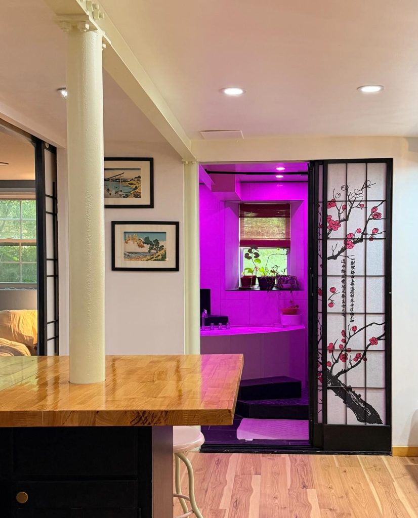 A black-framed sliding screen painted with plum blossom beside Japanese woodblock prints, with a butcher-block counter in the foreground.