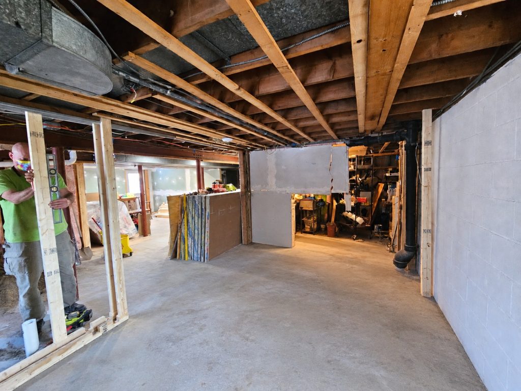Looking down the unfinished space during framing: concrete floor, new stud walls going up, concrete block on the right and stored materials beyond.
