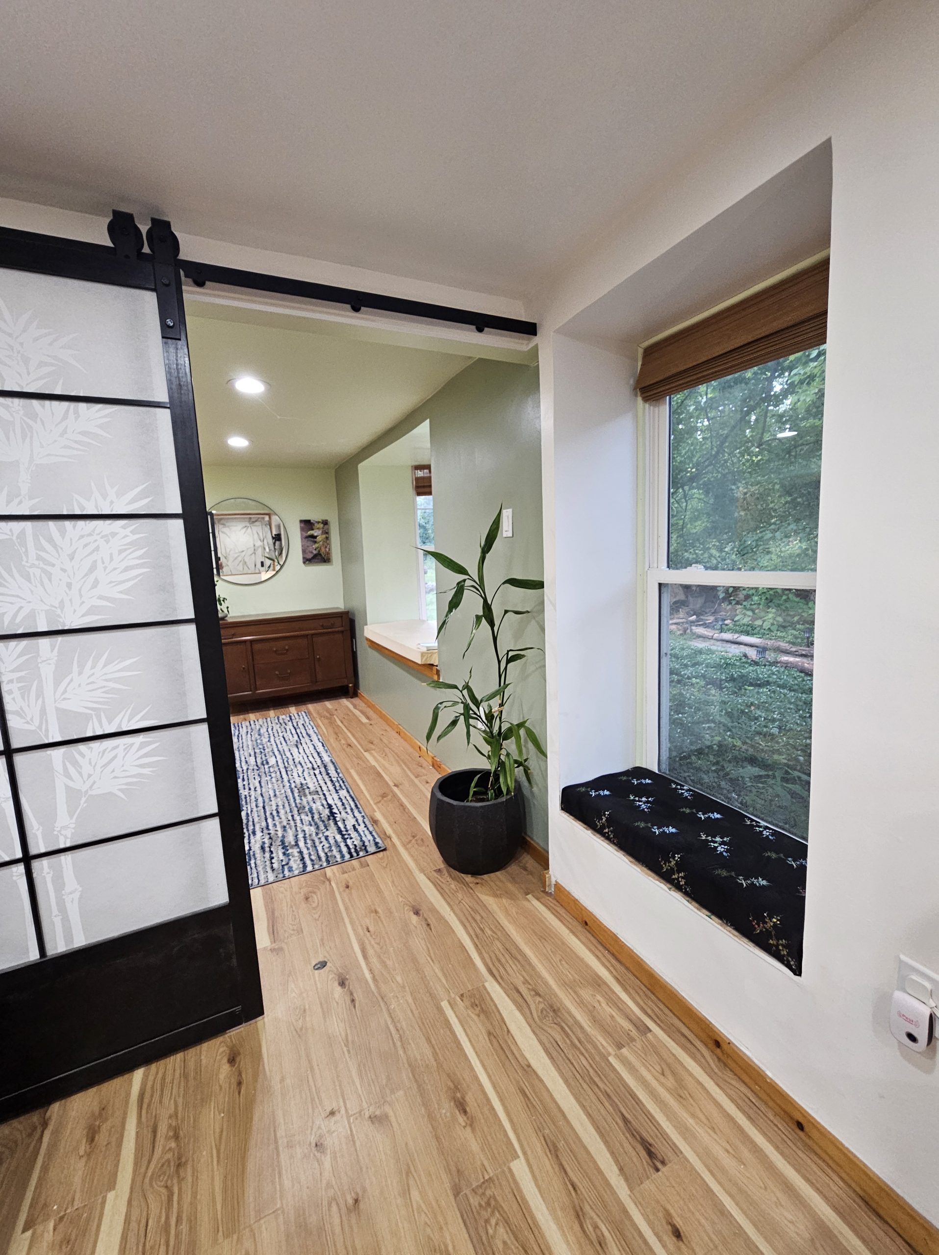 A shoji-inspired sliding door etched with bamboo beside a deep window seat, with oak floor and woods visible through the glass.