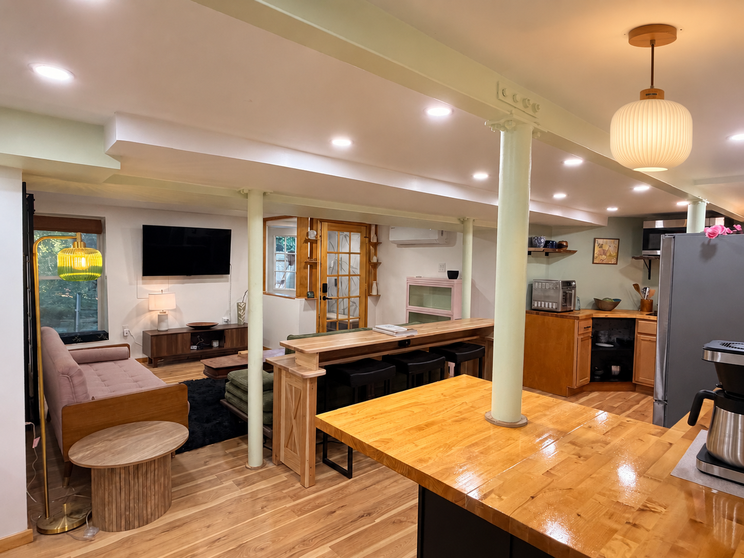 The finished Japandi apartment kitchen: a butcher-block counter spanning pale green columns, with a ribbed pendant lamp.