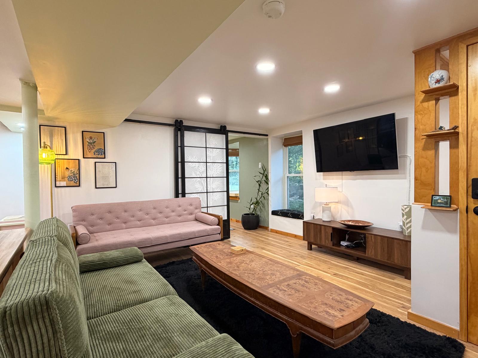 A finished basement apartment: warm oak floor, pale green walls, black-framed shoji screens and a butcher-block counter.