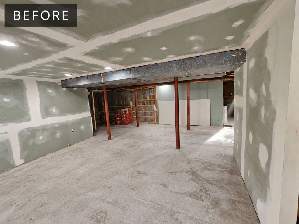 The living room area before work: bare concrete floor, red steel columns, taped drywall and exposed joists overhead.