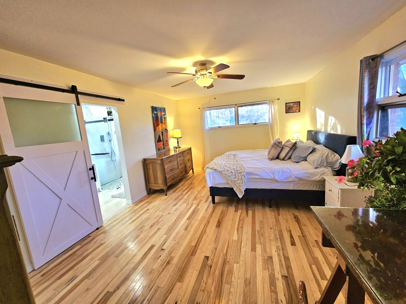 A bedroom with a sliding barn door, warm wood floor and low furniture kept below the window line.
