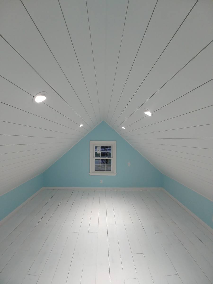 A finished attic with a white shiplap ceiling following the roof pitch, and a small gable window.