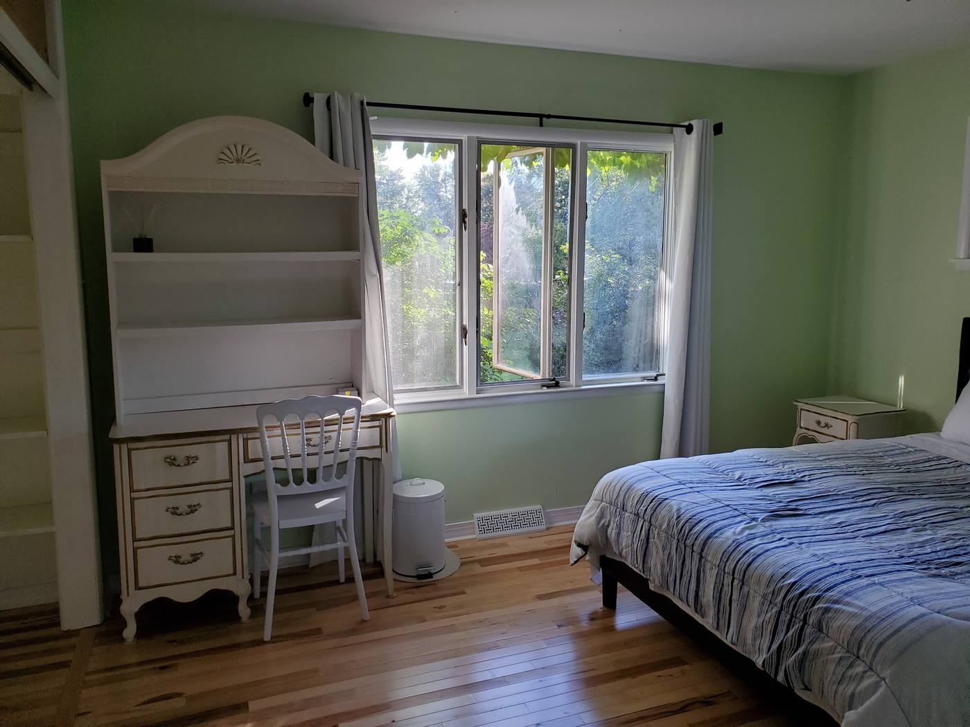A built-in desk under a window in a green bedroom, with trees beyond the glass.