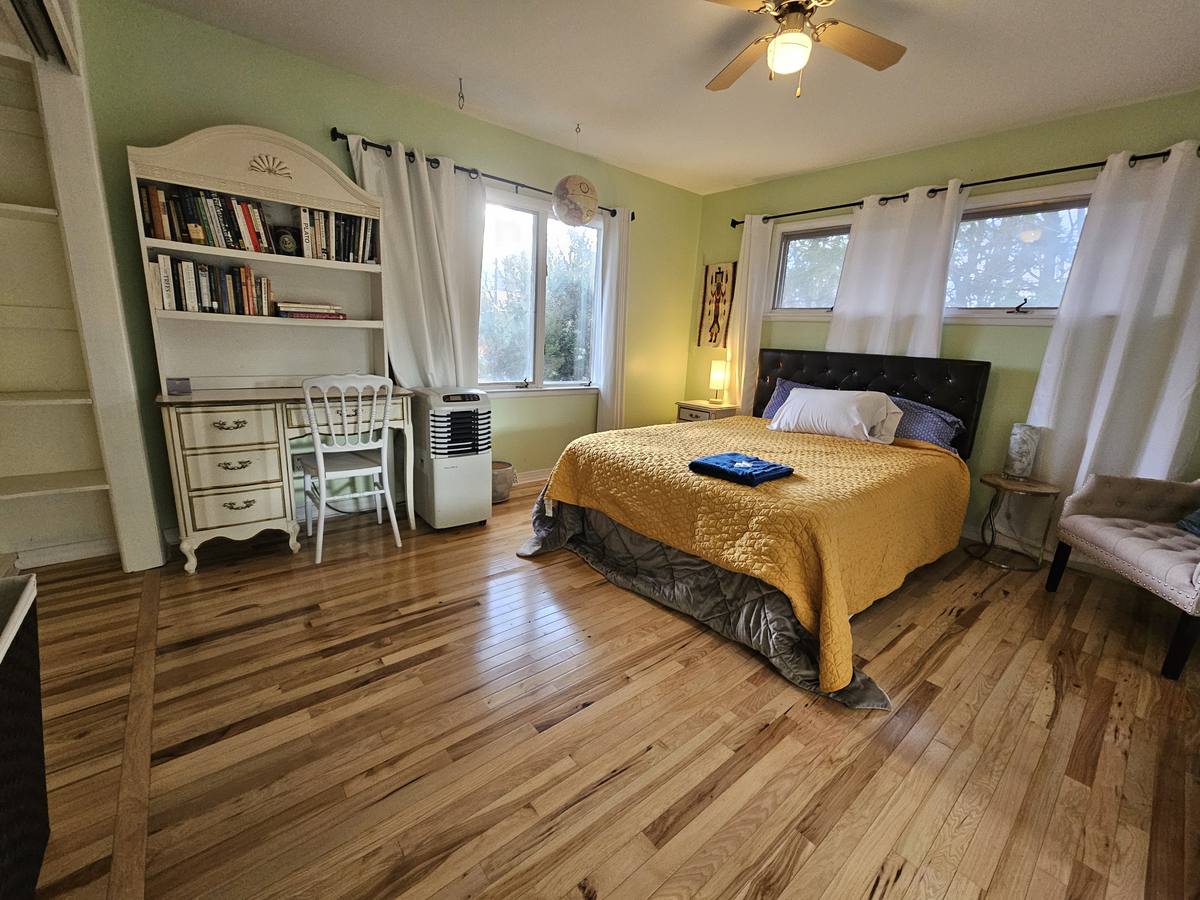 A green bedroom with built-in shelving and a desk beside the window, and a warm oak floor.