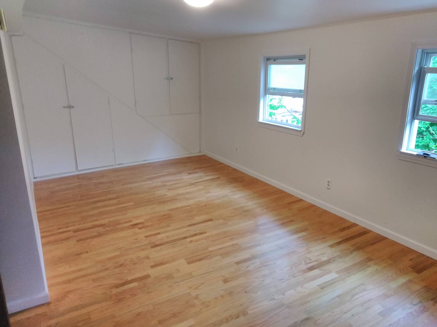 An empty room finished in white with a new oak floor, built-in cupboards and light from two windows.