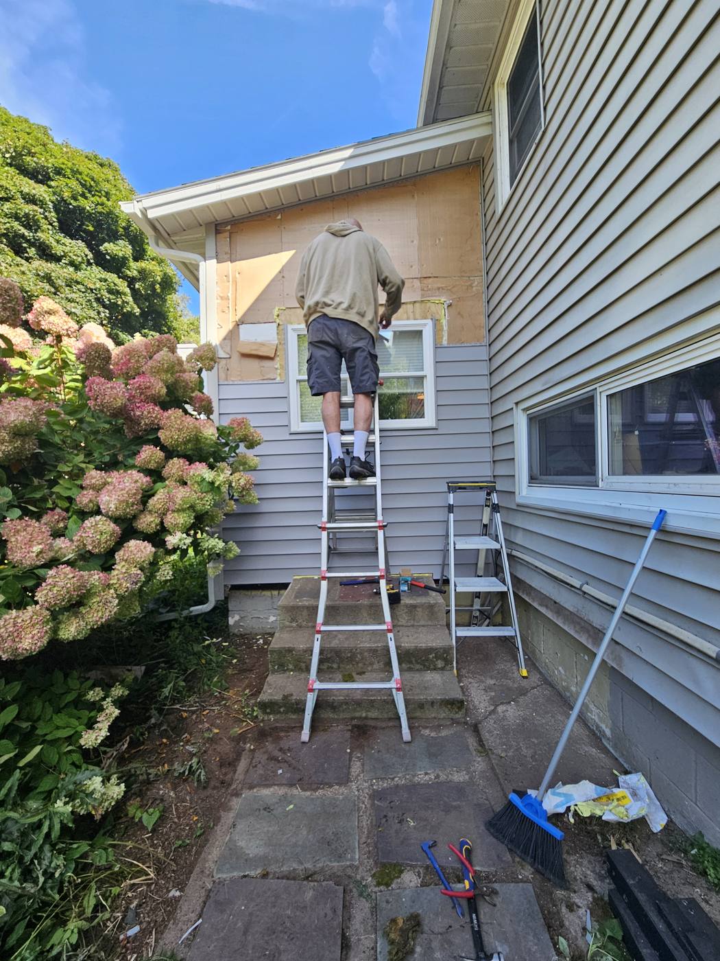 The outside of a house mid-project, with hydrangeas in bloom along a stone path.