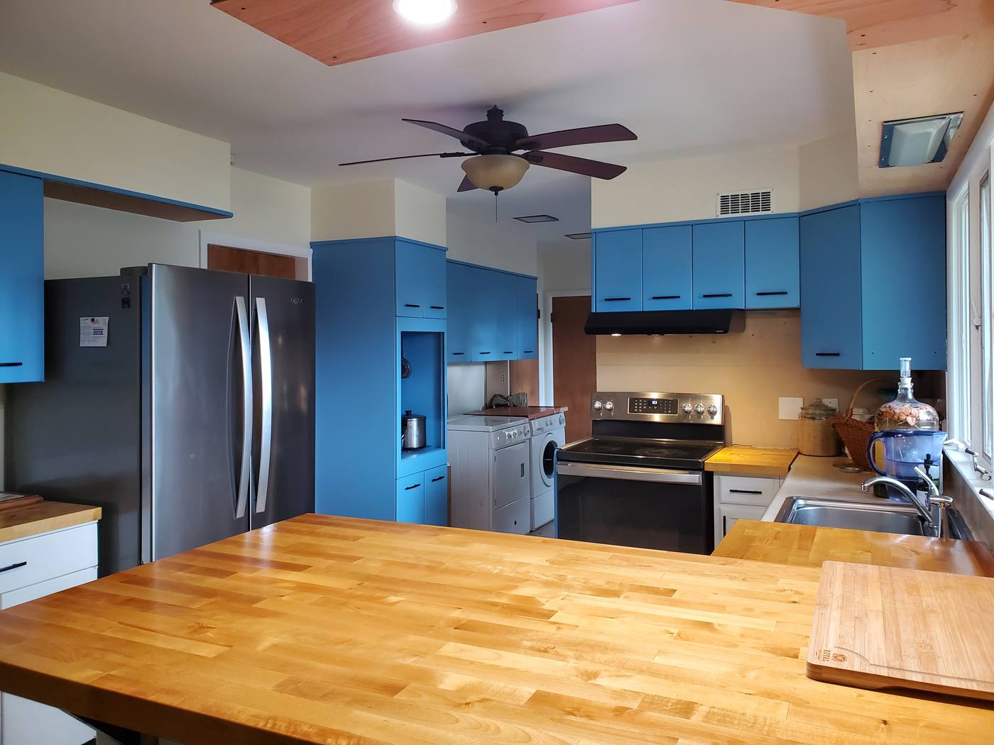 A kitchen with thick butcher-block counters, blue upper cabinets and stainless appliances.
